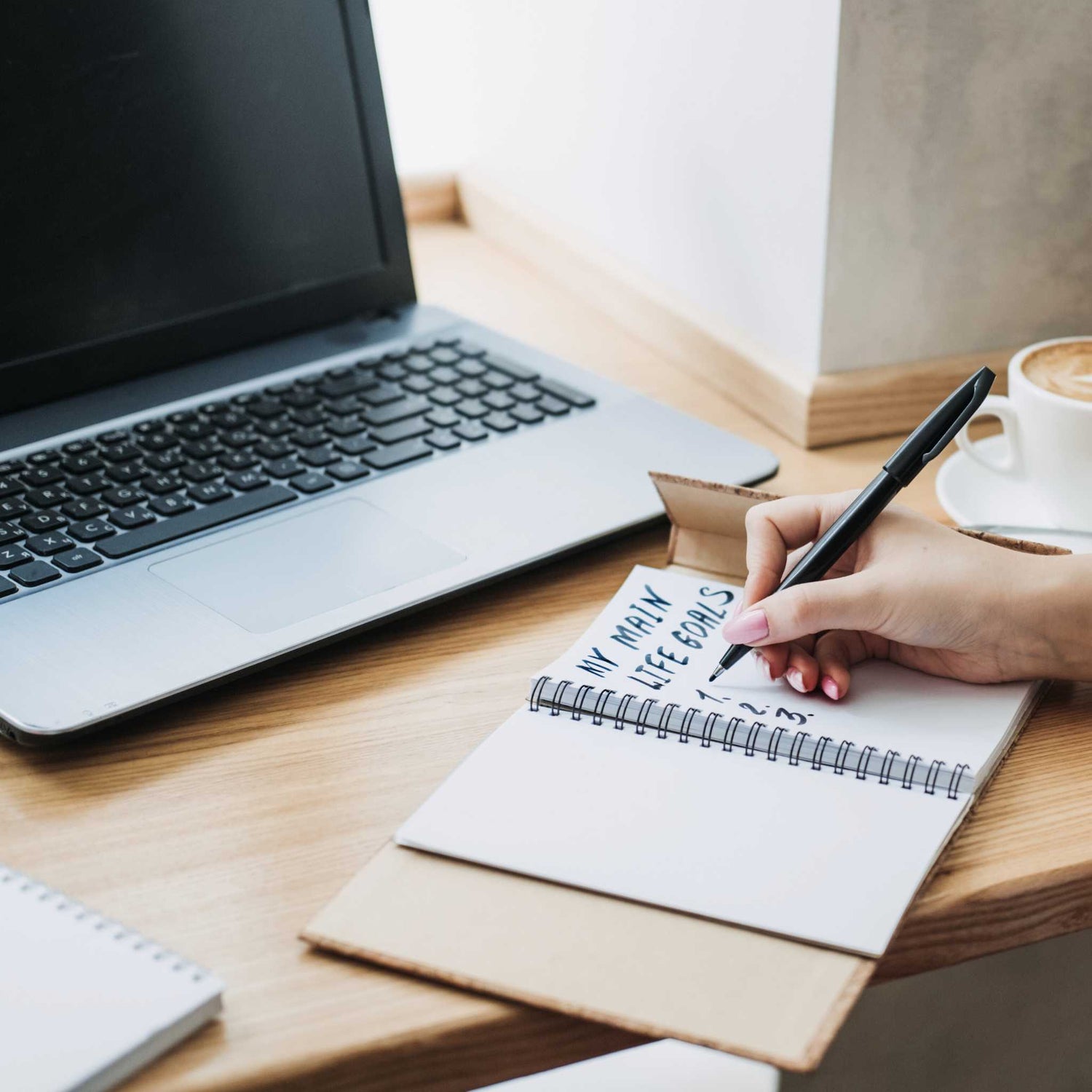 Person sitting at desk in front of computer writing list of life goals in notebook